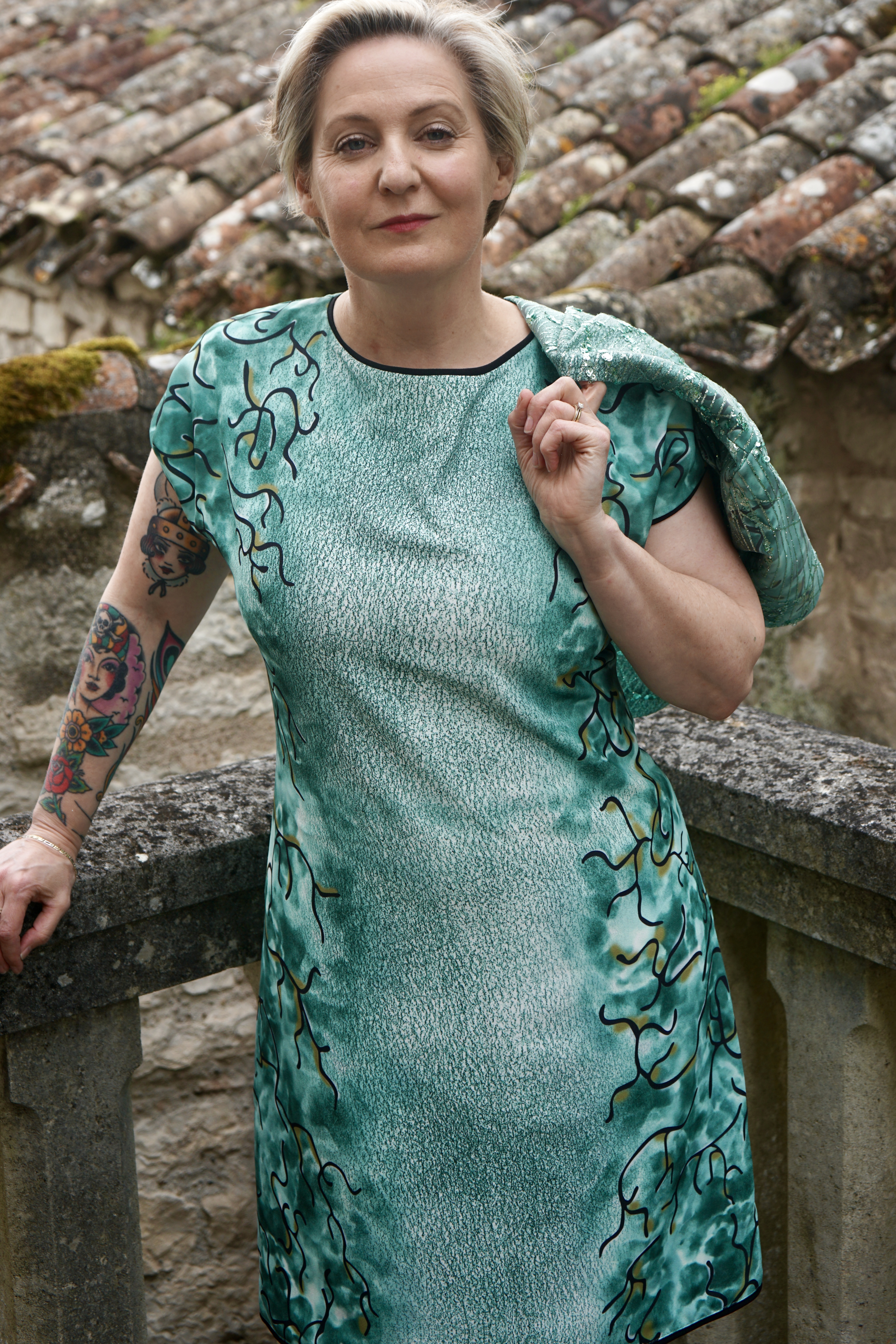 mannequin portant une robe de soirée verte de créateur sur mesure avec un boléro assorti, présentant des motifs entrelacés noirs et des broderies argentées inspirées de l'art rococo de Fragonard